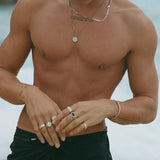A man with a bare torso on a beach, wearing the Billie Jo Onyx Ring and other silver jewellery.