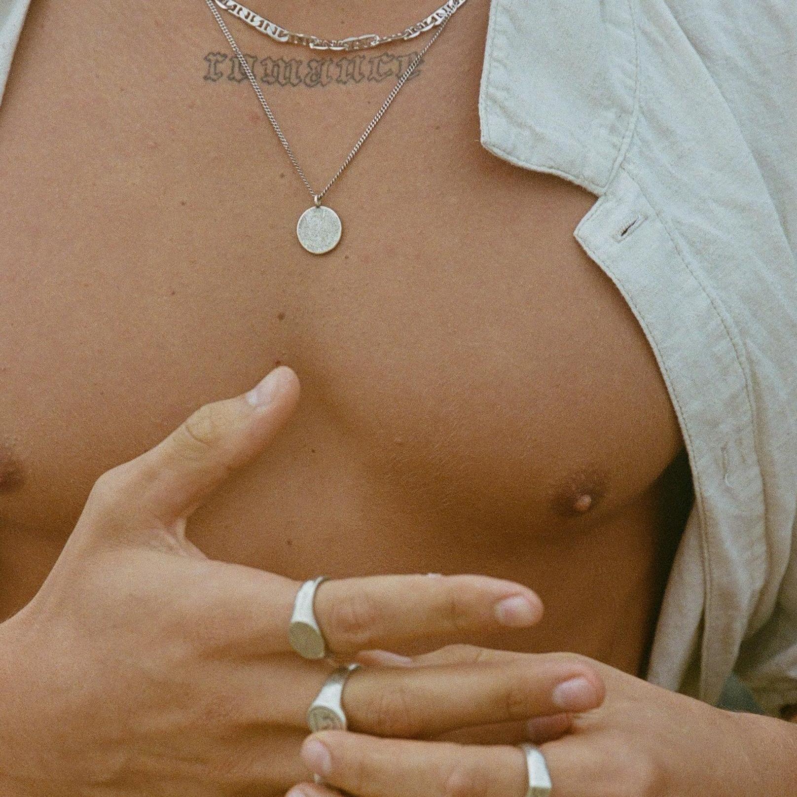 A close-up of a man's chest, showing the sterling silver Untold Pendant from Billie Jo layered with a thicker chain for a modern, stylish look.