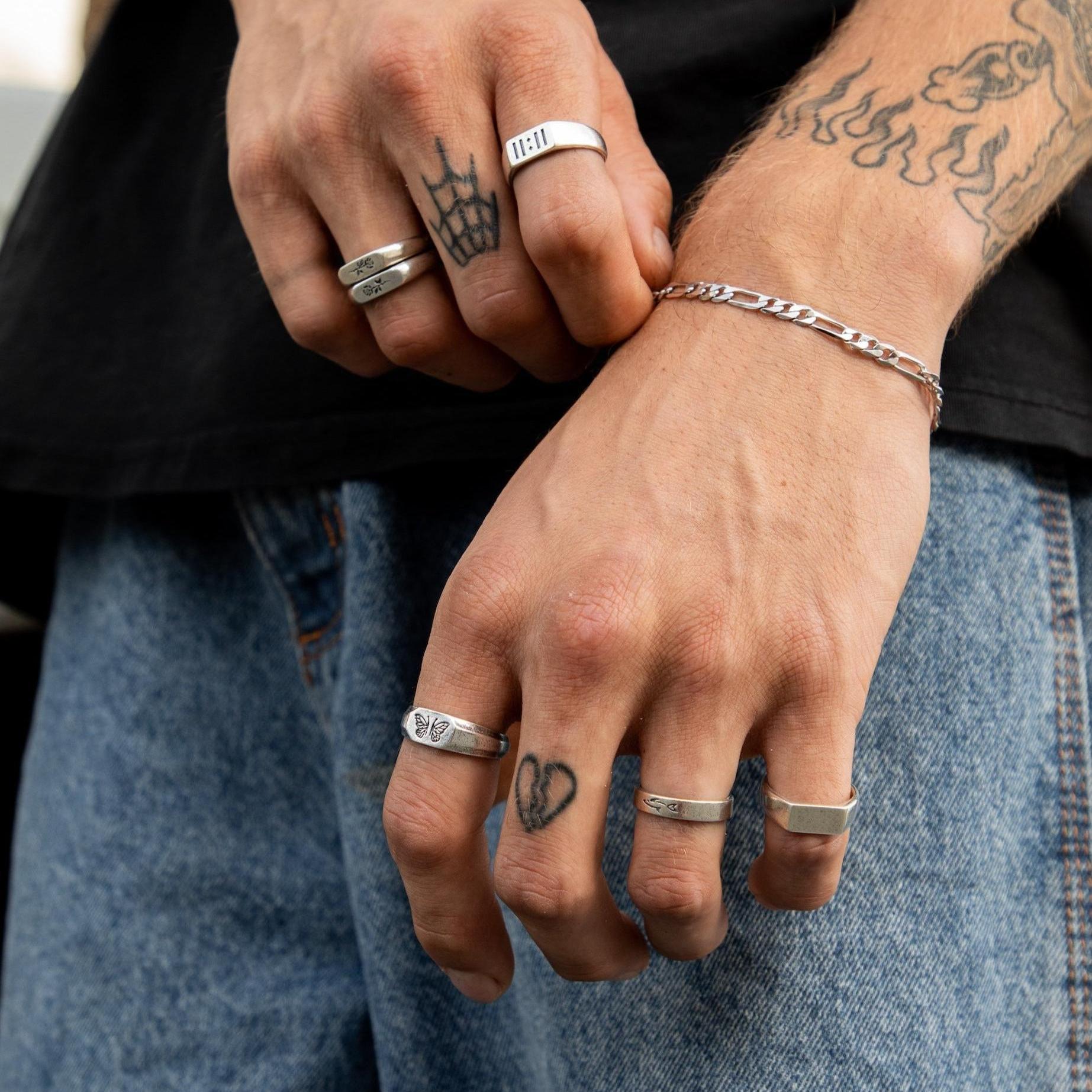 A man with tattooed hands wears a stack of sterling silver rings from Billie Jo, including the Prowess Ring, paired with a silver chain bracelet for a modern, layered look.