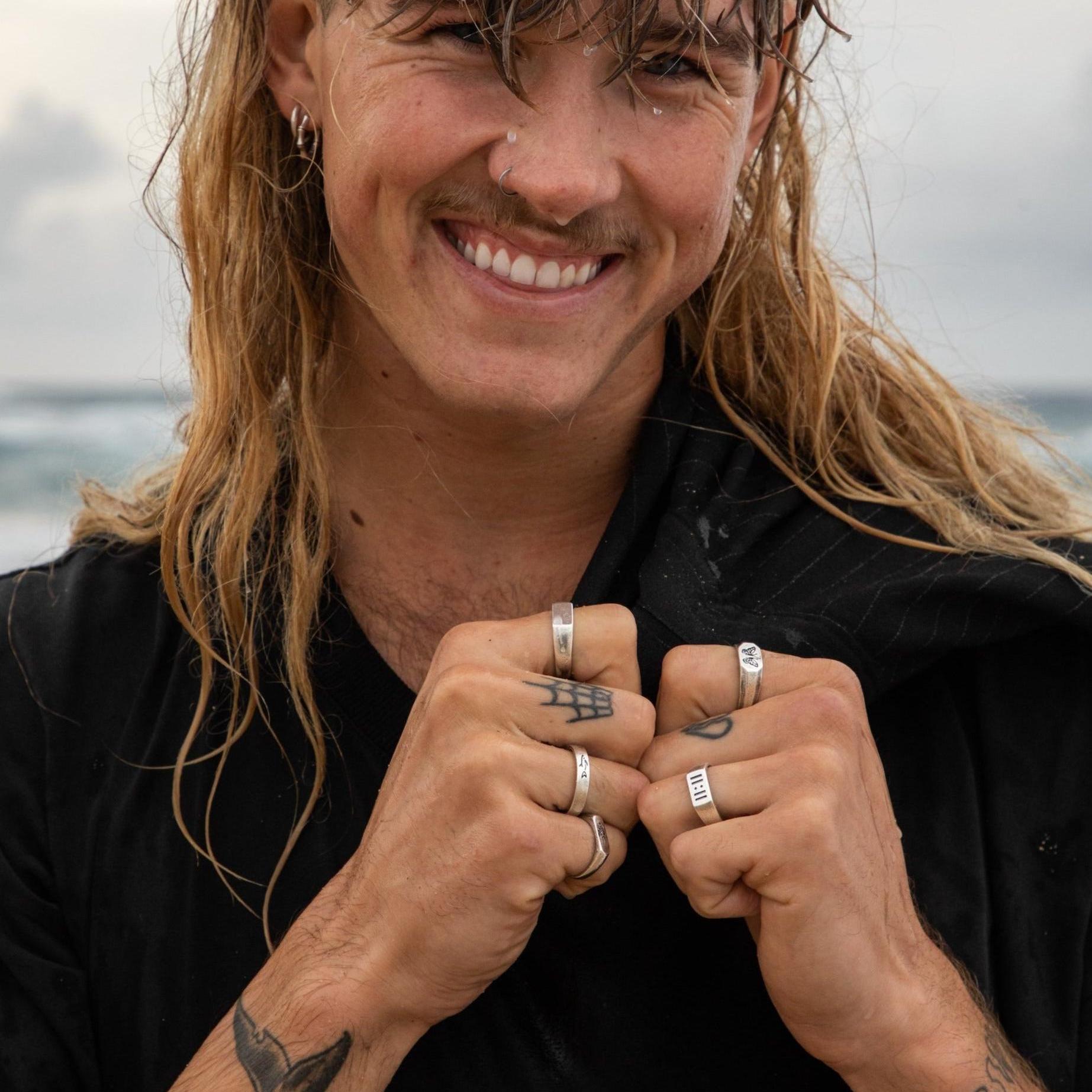 A smiling man on a beach wearing the Billie Jo Revival Ring. A campaign shot with a coastal, relaxed vibe, showcasing the Australian brand's aesthetic.