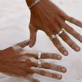 A man's hands, dusted with white sand, wearing a stack of sterling silver rings from Australian men's jewellery brand Billie Jo, including the Union Ring.
