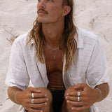 A man with long, sandy hair wearing a selection of Billie Jo men's jewellery, including the sterling silver Forge Ring, for a relaxed, coastal aesthetic.
