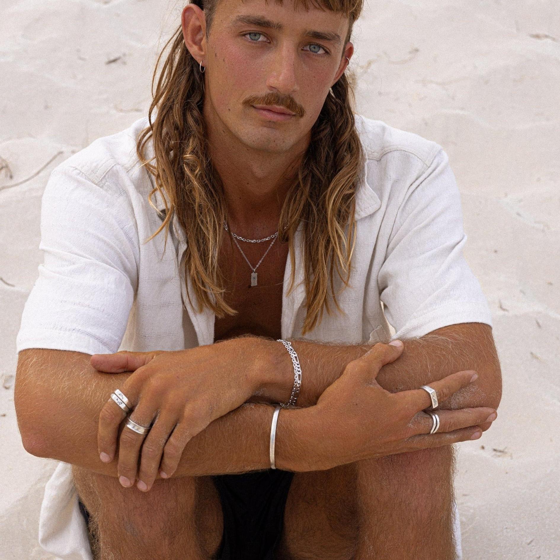 A model with a mullet and moustache wears the Billie Jo Drifter Cuff and other silver jewellery, embodying a cool, coastal Australian vibe.