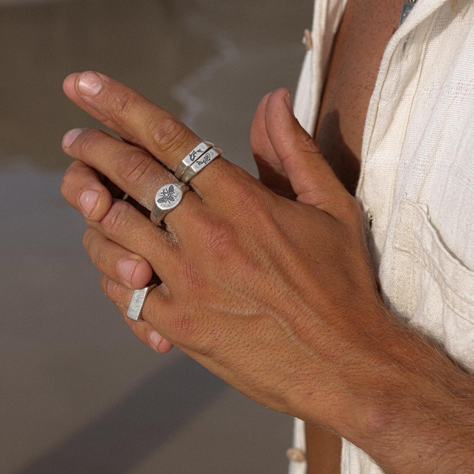 A close-up of a man's hand wearing the Billie Jo BEE THERE RING, styled with other silver rings, showcasing its unique, modern design.
