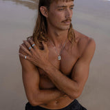 A male model on a Gold Coast beach wearing the sterling silver BEE THERE RING and other layered jewellery from Australian brand Billie Jo.