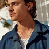 A male model wearing the sterling silver Paradiso Pendant from Billie Jo, styled with a white tank top and an open blue shirt for a casual look.