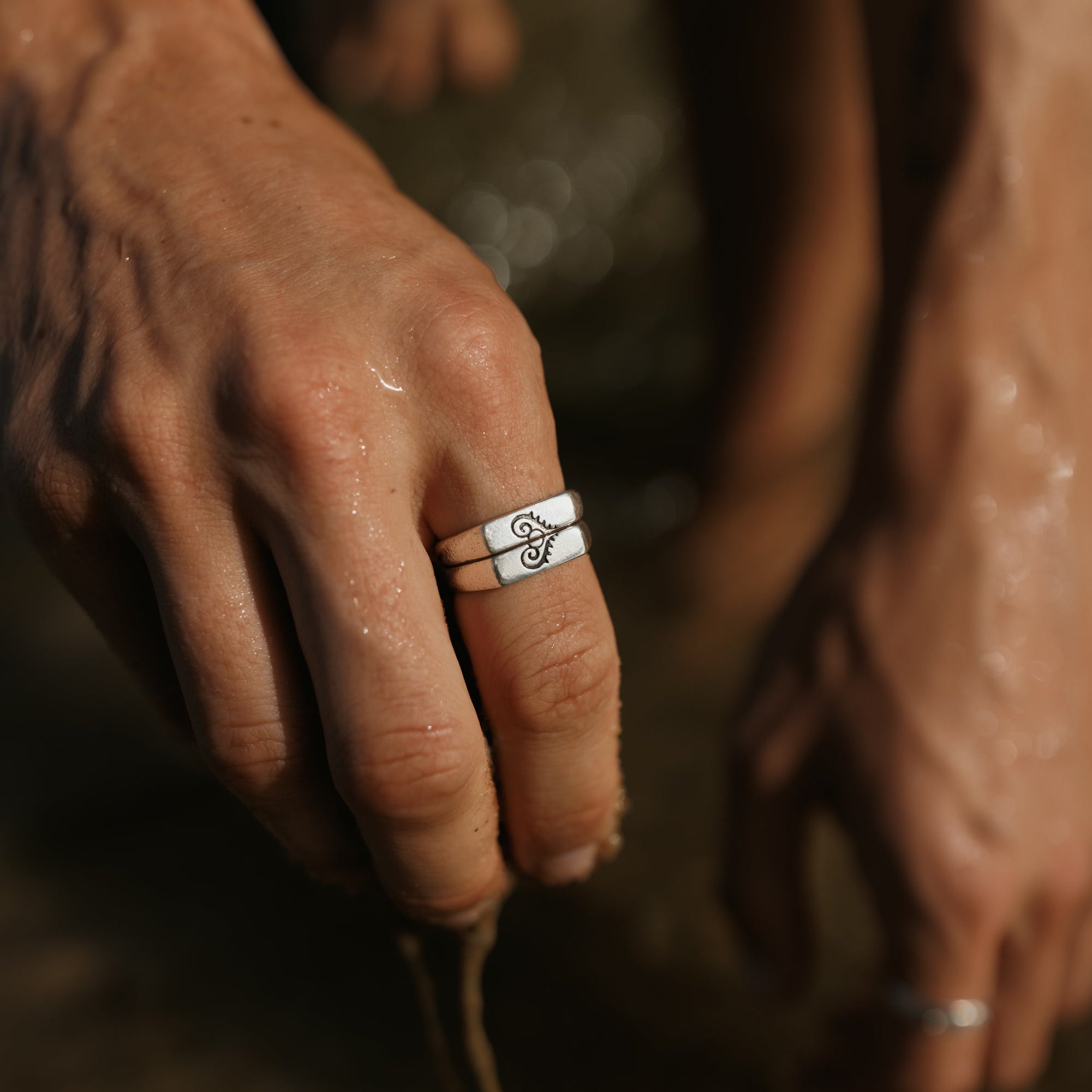 Close-up of the Billie Jo Connection Stackers on a man's hand, with a wet, sandy background. Durable men's sterling silver jewellery.