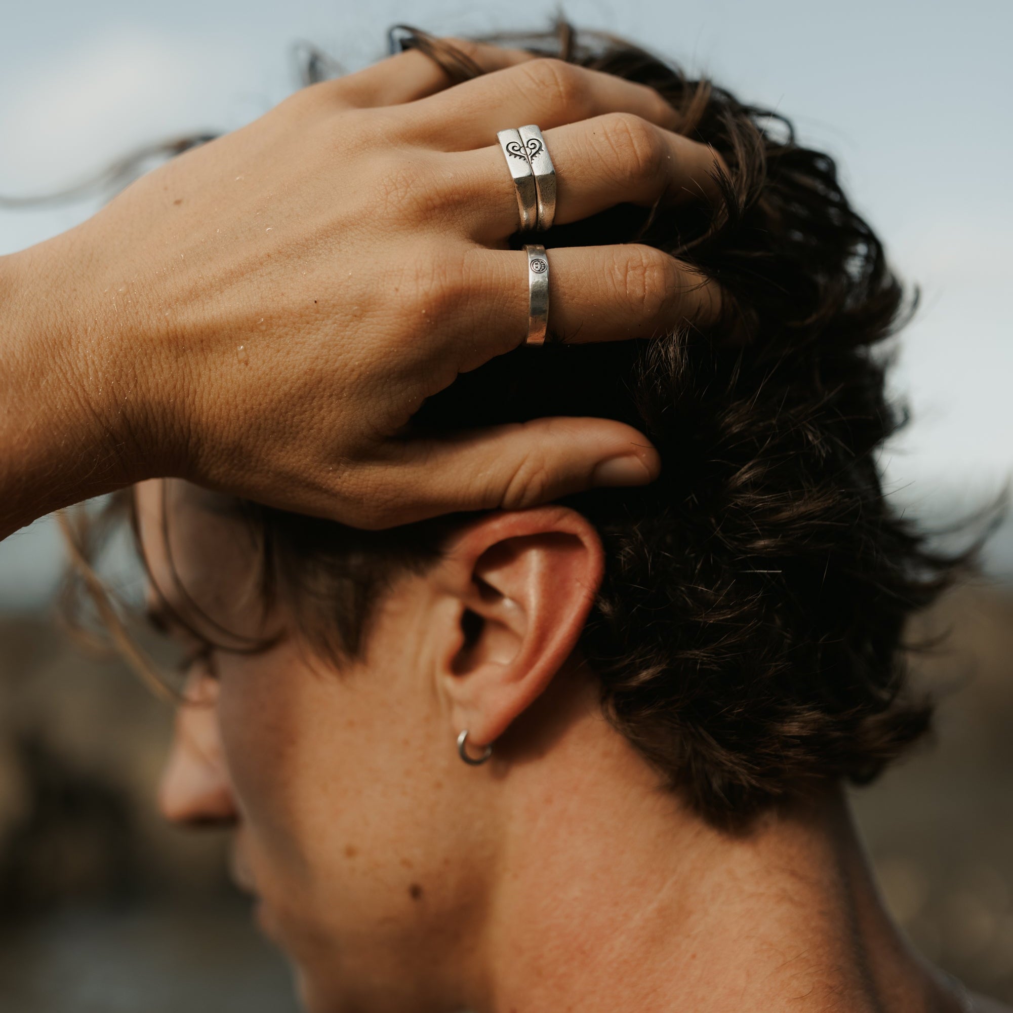 Close-up of a man's hand wearing the Billie Jo Reflection Ring and a stacked silver ring, running through his hair. An editorial shot with a modern, masculine feel.