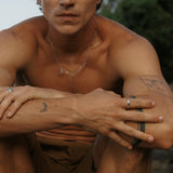 A man wearing the Billie Jo Reflection Ring on his right hand, part of a stylish, layered jewellery look with a silver necklace and other rings.