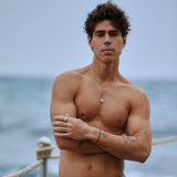 A man models the Billie Jo Untold Pendant on a beach, showcasing the sterling silver necklace against his chest for a modern, masculine look.