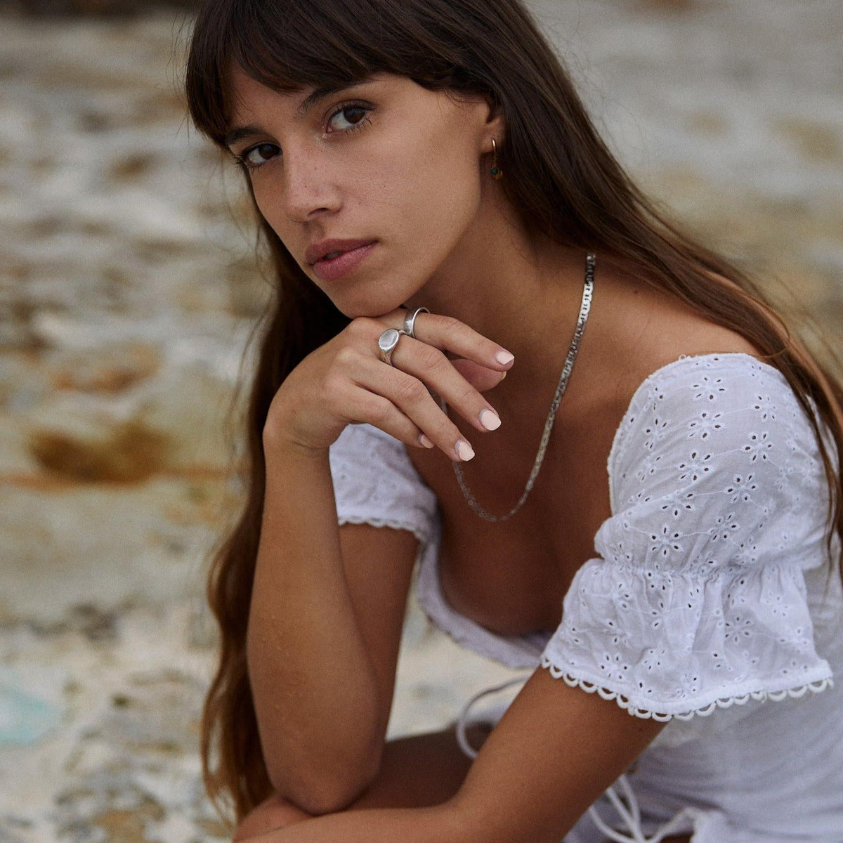 A woman with long brown hair wearing the silver Signet Ring by Billie Jo, paired with a delicate silver necklace and a white broderie anglaise top.
