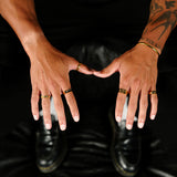 An editorial shot of a man's hands adorned with several gold rings from Billie Jo, including the Union Ring, against a dark, moody background.