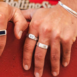 A close-up of a man's hands wearing the Billie Jo Canvas Ring and other sterling silver rings, resting on a red surface. Australian men's jewellery.