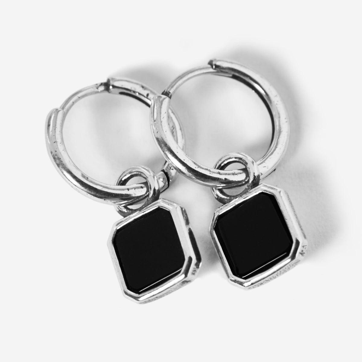 A pair of sterling silver Nox Earrings by Billie Jo, featuring a small huggie hoop with a dangling geometric black stone pendant on a clean white background.