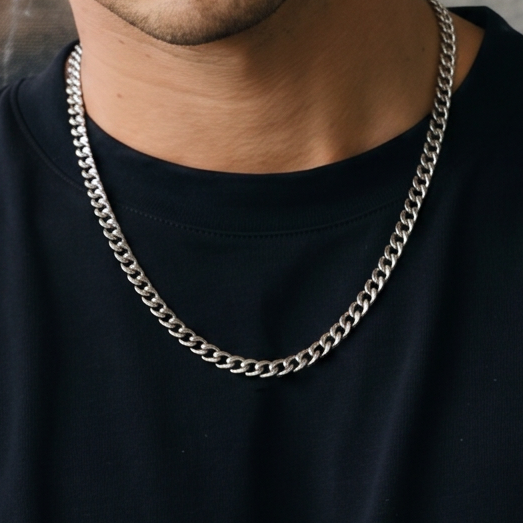Man wearing a black t-shirt and silver chain necklace against a textured gray wall.