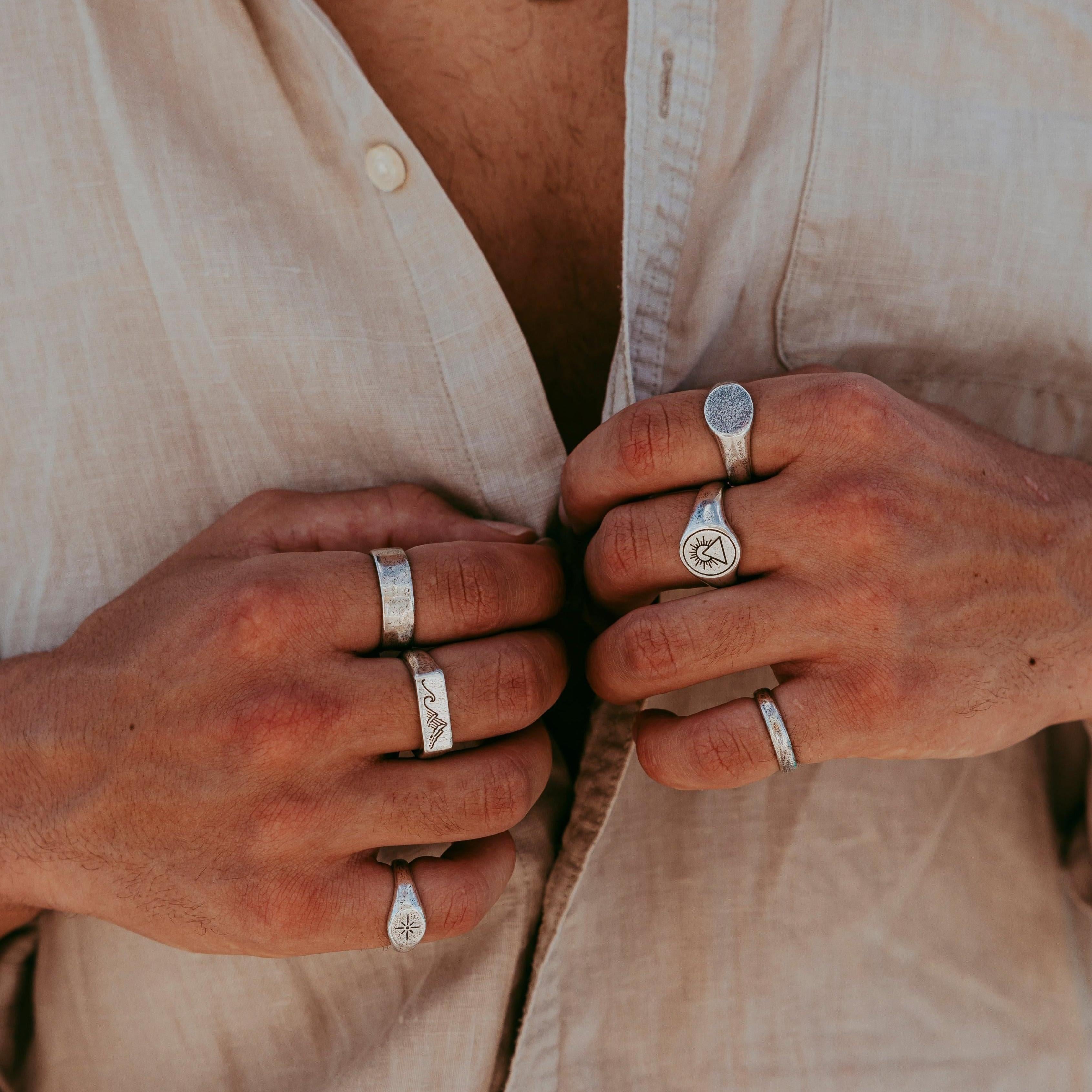 A man wearing a collection of sterling silver rings from Billie Jo, including the Union Ring, against a neutral-toned linen shirt. Modern men's jewellery.
