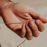A close-up of a man's hand holding the delicate sterling silver Snake Necklace from Billie Jo, showcasing its smooth texture and quality craftsmanship.