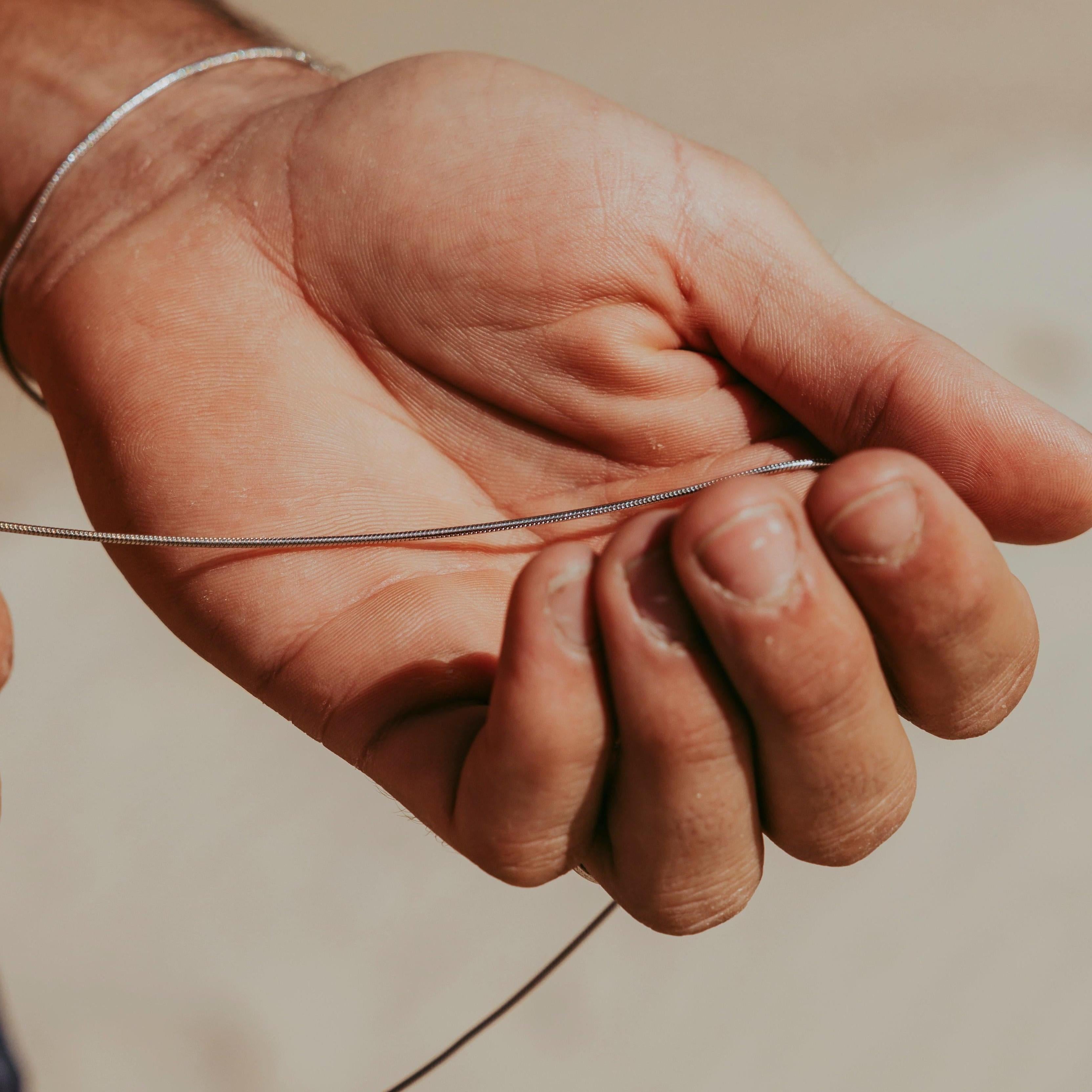 A close-up of a man's hand holding the delicate sterling silver Snake Necklace from Billie Jo, showcasing its smooth texture and quality craftsmanship.