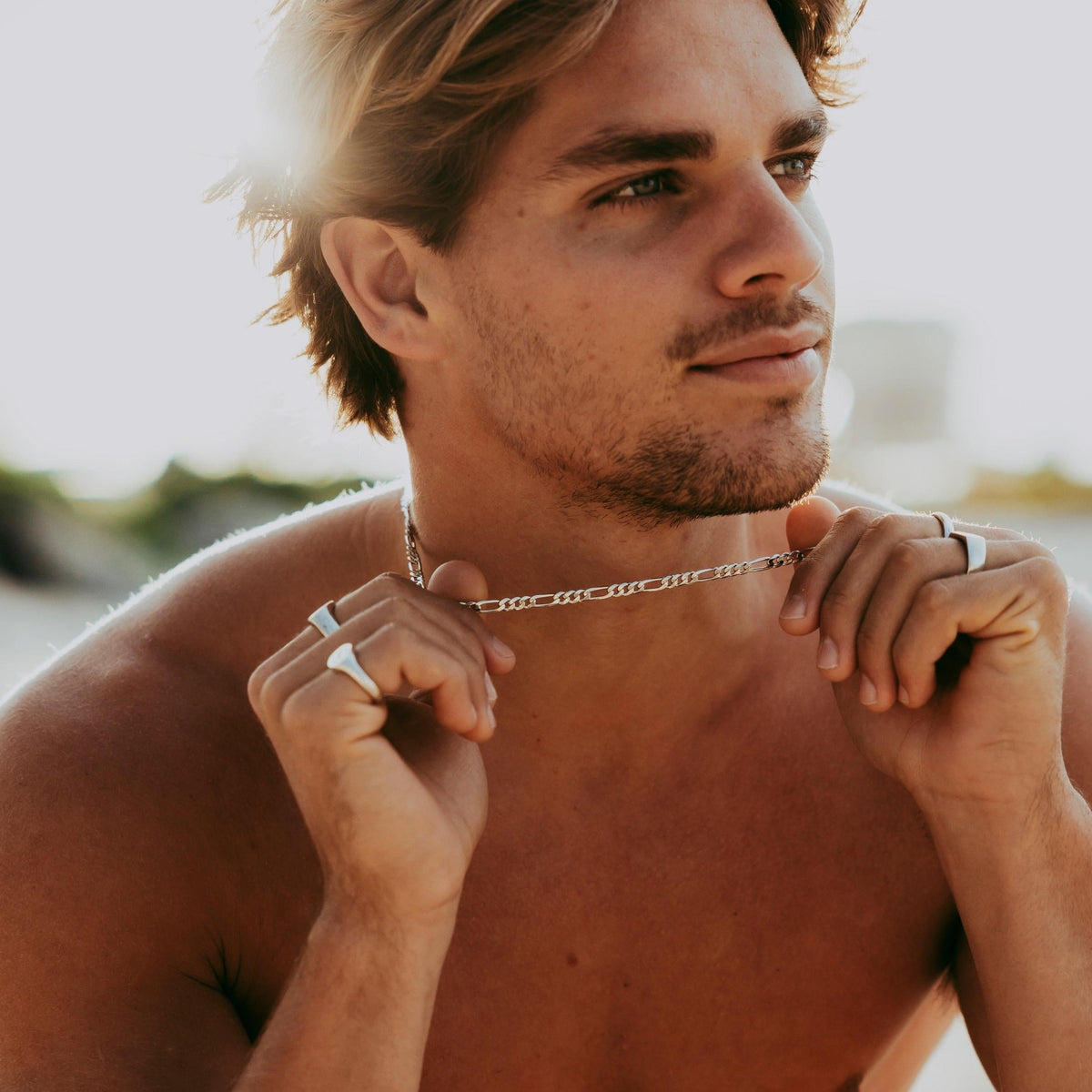 A man with sun-kissed hair puts on the sterling silver Figaro Necklace from Billie Jo. A modern, masculine piece of men's jewellery for everyday wear.