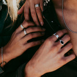 A man wears the sterling silver Billie Jo ONYX 2.0 RING in a close-up shot. Another hand with rings rests on his shoulder, highlighting the jewellery.