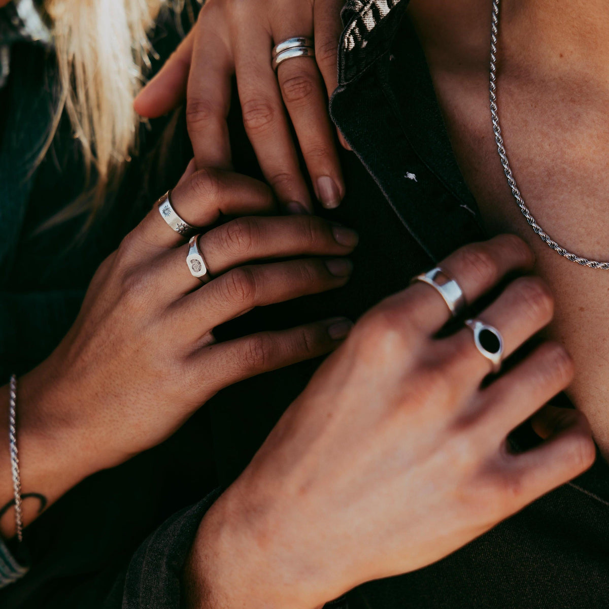 A close-up of a man wearing the sterling silver Rope Necklace from Billie Jo, layered with other silver rings and chains for a modern, styled look.