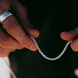 A close-up of a man's hands holding the Billie Jo Rope Necklace, showing the texture and detail of the sterling silver chain.