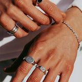 A close-up of a man's hands as he fastens a sterling silver Rope Bracelet from Billie Jo. He also wears several silver rings, showcasing a modern, layered jewellery style.