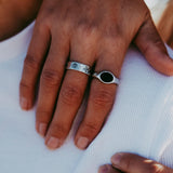 A close-up on-hand shot of the Billie Jo ONYX 2.0 RING, styled with another silver band on a man's hand against a white textured shirt. Australian men's jewellery.