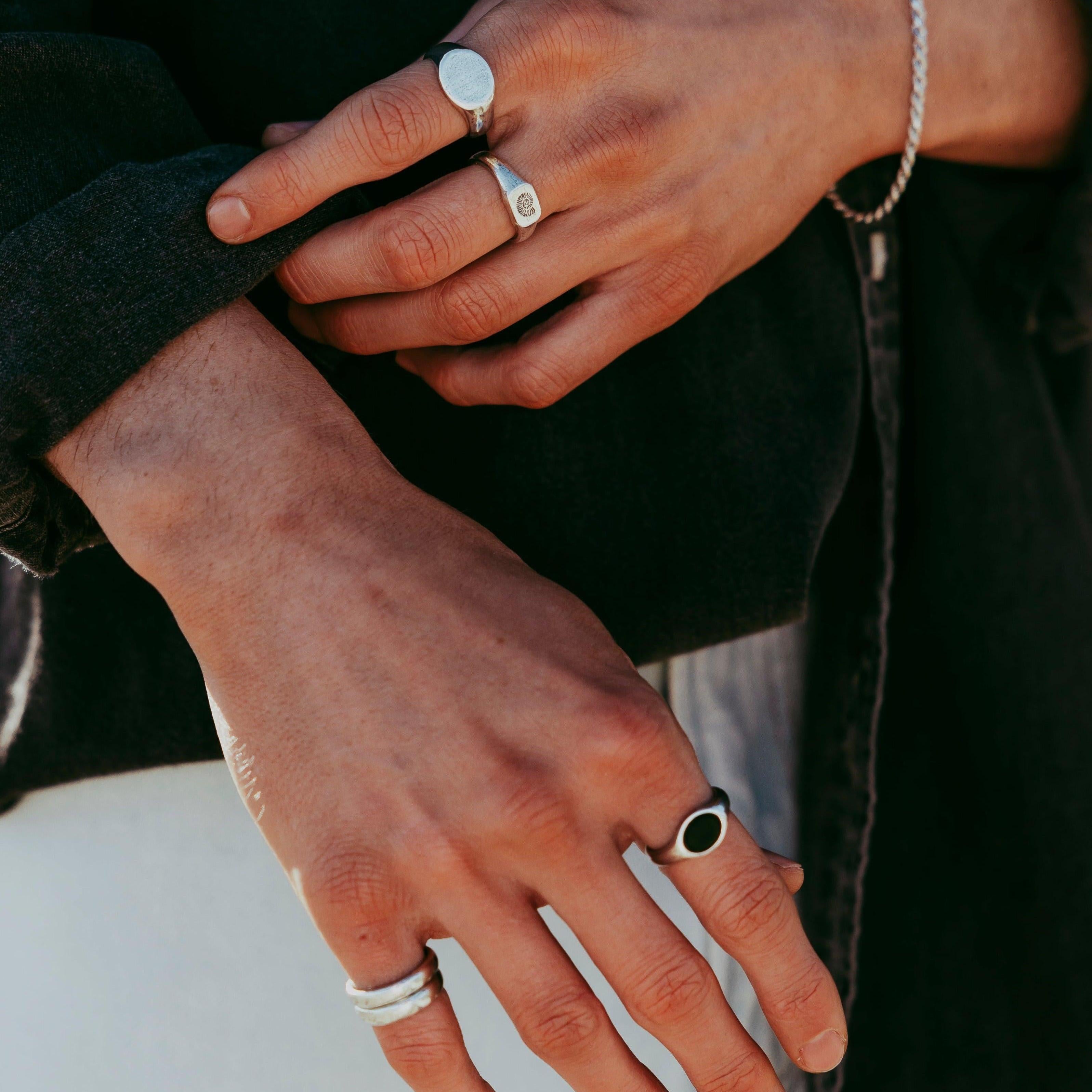 Two hands adorned with men's sterling silver rings from Billie Jo. The lower hand features the ONYX 2.0 RING, while the upper hand adjusts a dark sleeve, showcasing a stack of rings.