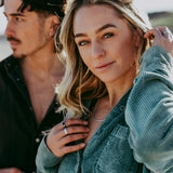 A woman with blonde hair wears the Billie Jo Rope Necklace, layered over a green corduroy shirt, showcasing the brand's versatile and stylish men's jewellery.