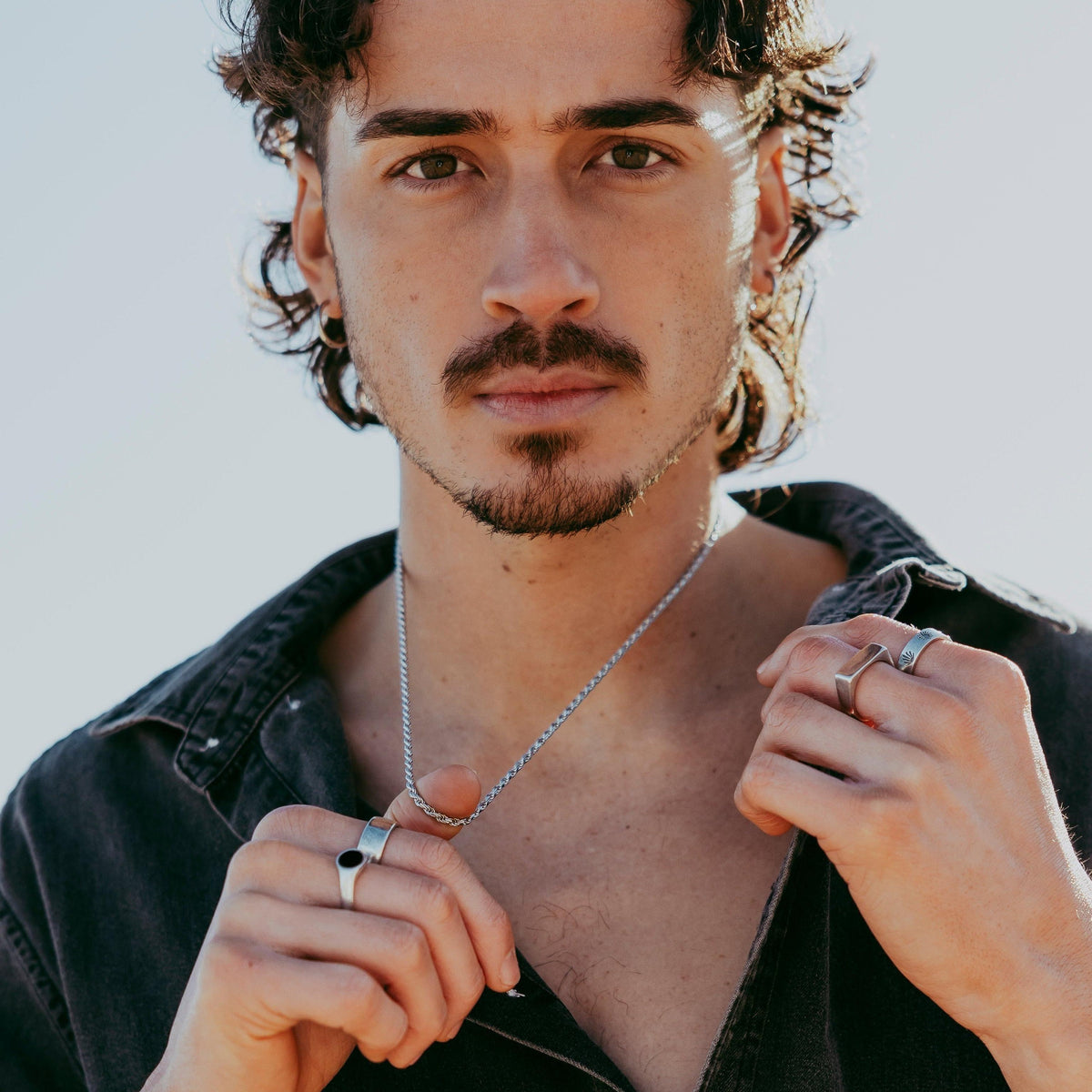 A male model with curly dark hair wears the Billie Jo Rope Necklace with a black button-up shirt, showcasing the brand's modern and masculine aesthetic.
