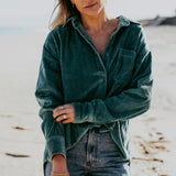 A woman on a beach wearing a Billie Jo sterling silver Rope Bracelet, paired with a casual green corduroy shirt and denim jeans for a relaxed, coastal look.