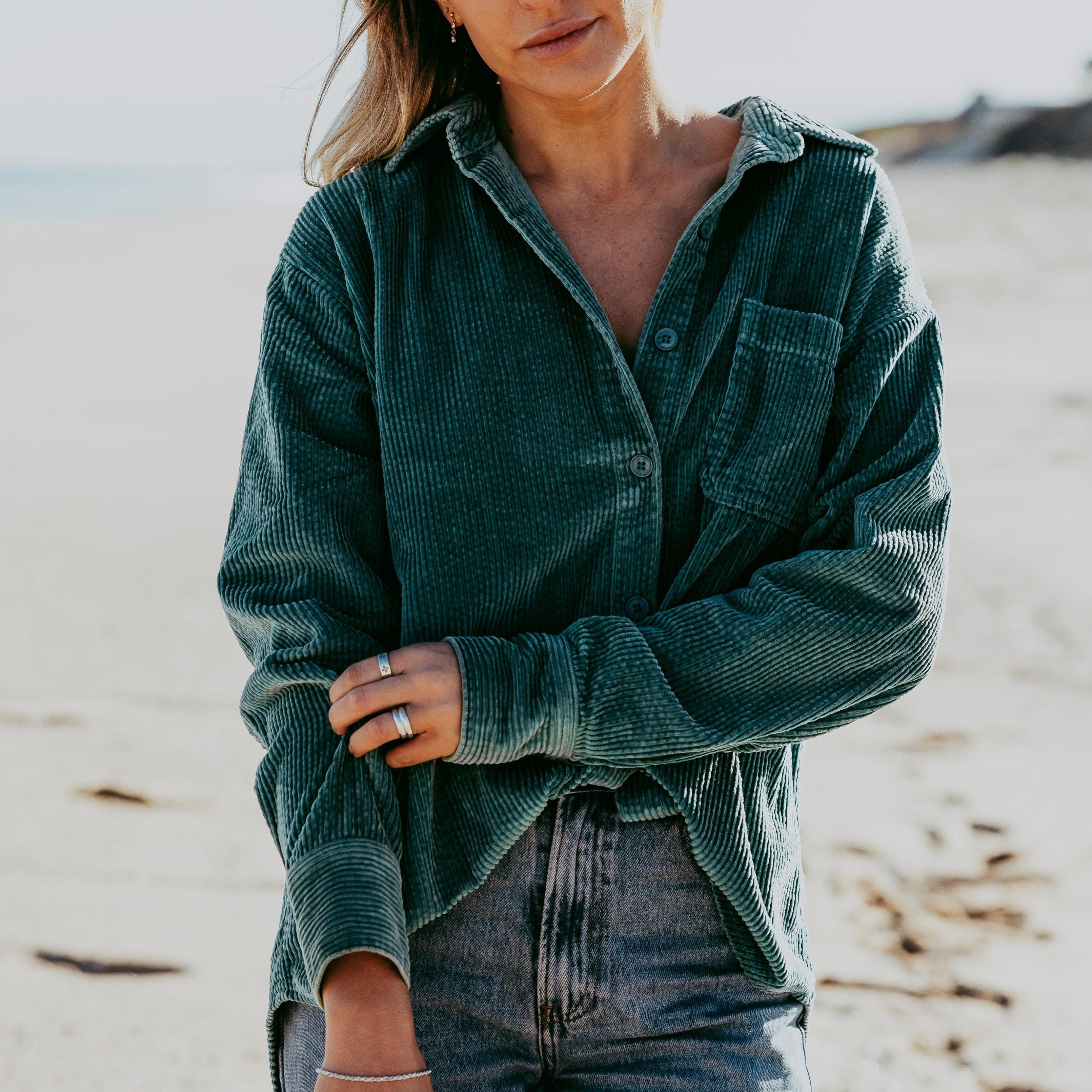 A woman on a beach wearing a Billie Jo sterling silver Rope Bracelet, paired with a casual green corduroy shirt and denim jeans for a relaxed, coastal look.