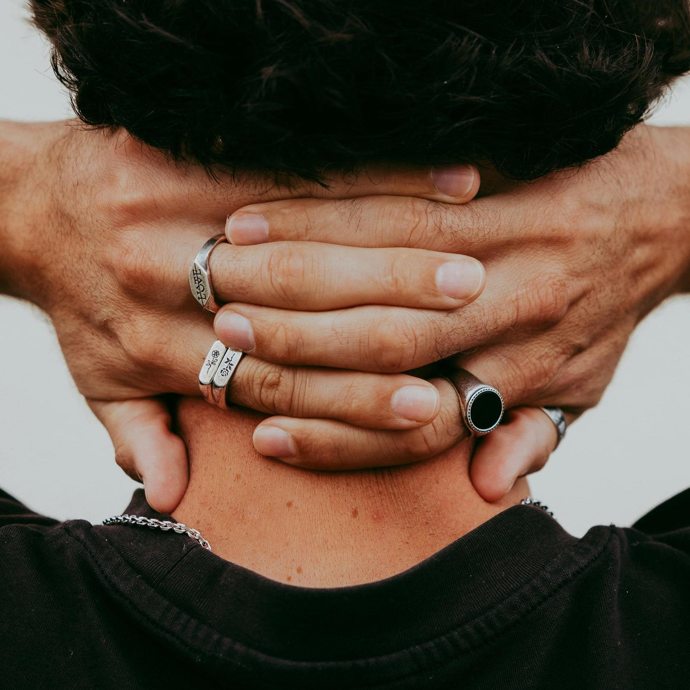 A close-up of a man's hands behind his head, showcasing a collection of sterling silver rings from Australian brand Billie Jo. The Rosa II ring is visible on his right hand.