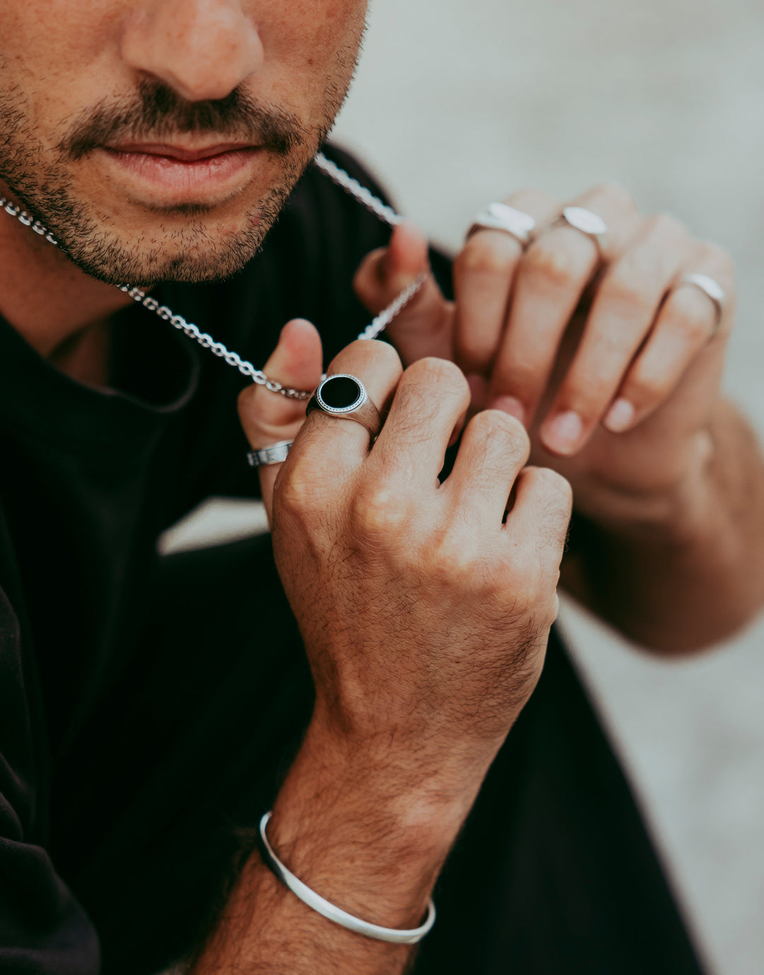 Man wearing the Abyss Ring with black onyx stone while adjusting a silver necklace, showcasing a minimalist jewellery style