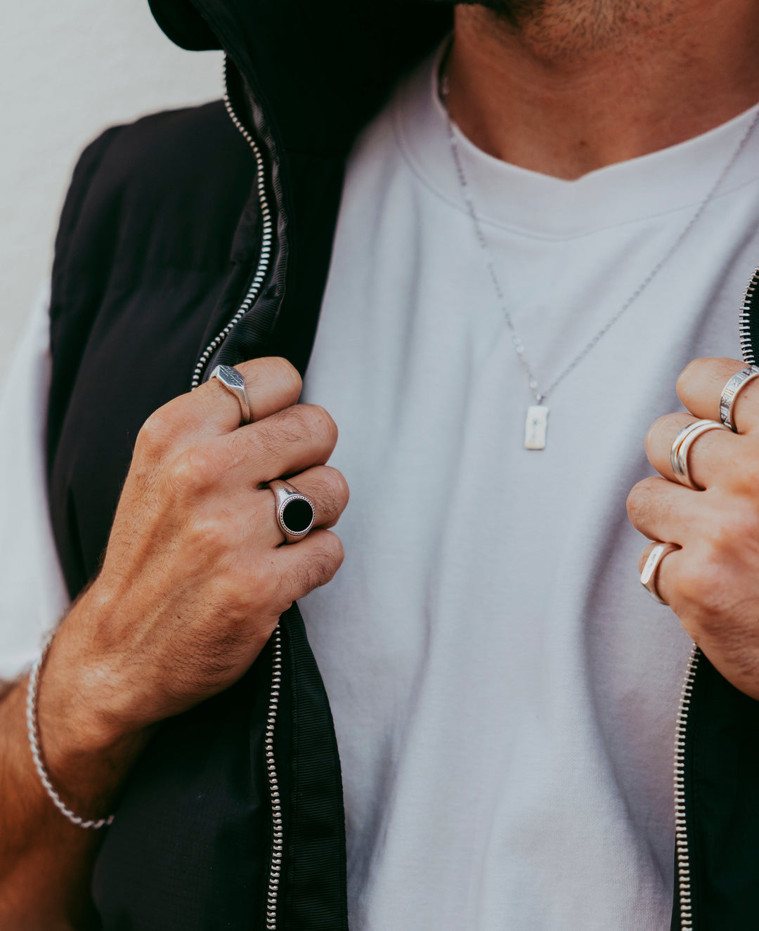 Man wearing the Abyss Ring with black onyx stone along with other silver rings and a necklace, styled with a casual outfit