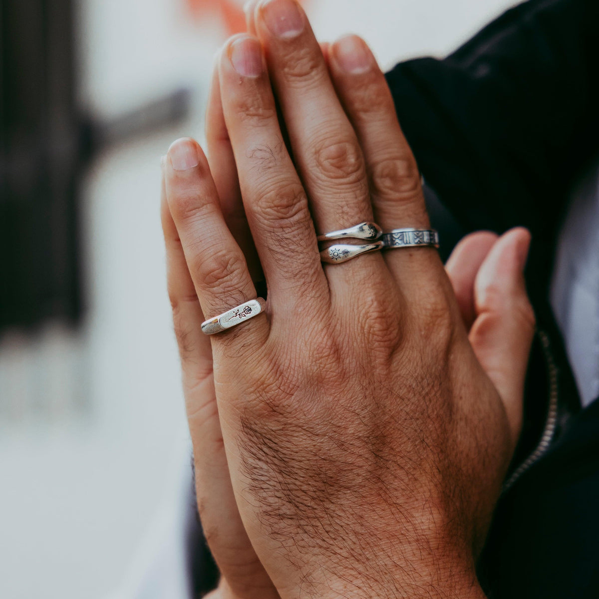 A man's hands clasped together, wearing the Rosa II ring on his little finger. A lifestyle shot for Billie Jo showing how the ring can be styled with other jewellery.