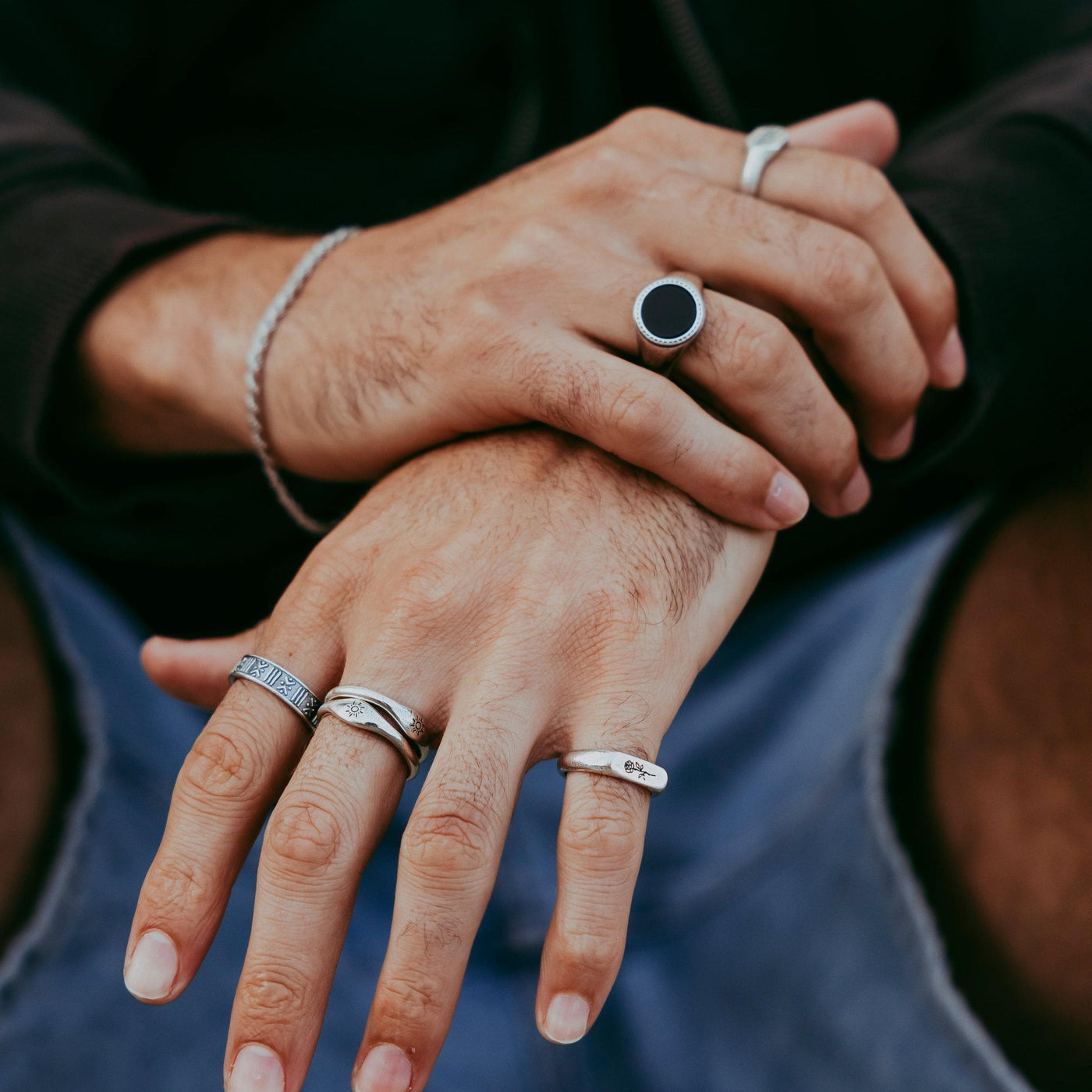 A man's hands styled with multiple silver rings from Billie Jo. The Rosa II Ring is on the ring finger, showing how this sterling silver piece complements other jewellery.