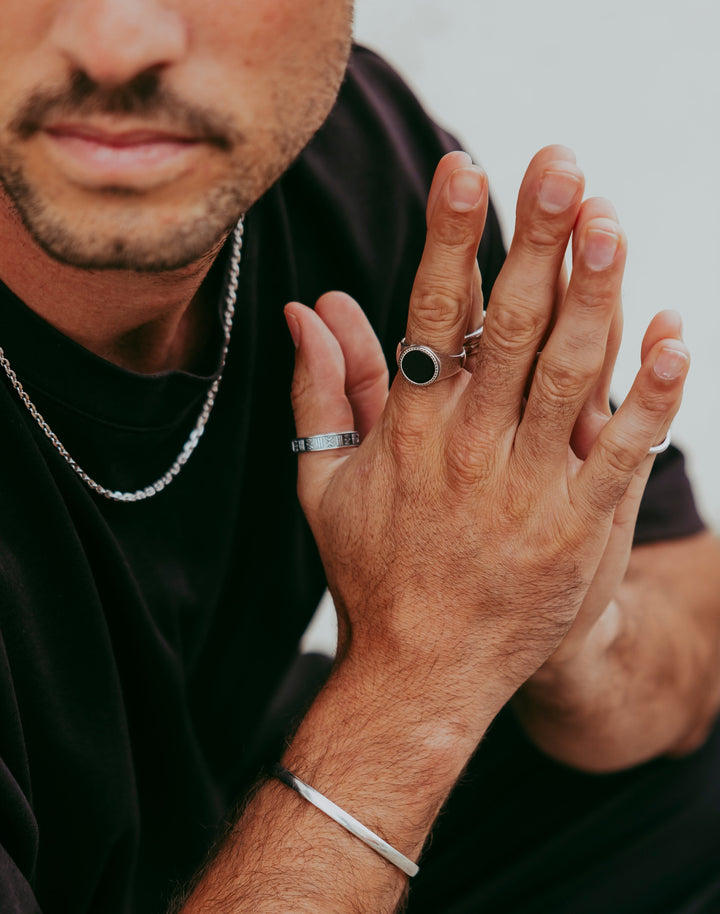 Man showing hands while wearing the Abyss Ring with black onyx stone and multiple silver rings, minimalist jewellery style