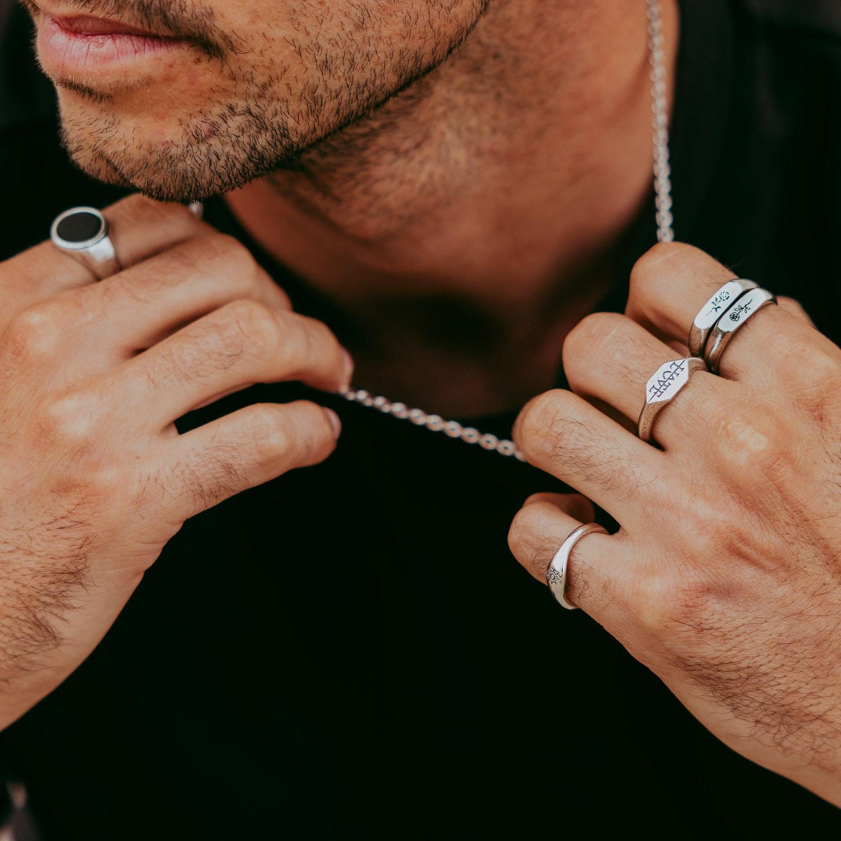 A close-up of a man's hands, showcasing the sterling silver Rosa Stacker rings by Billie Jo, styled with a silver chain and other rings for a layered jewellery look.