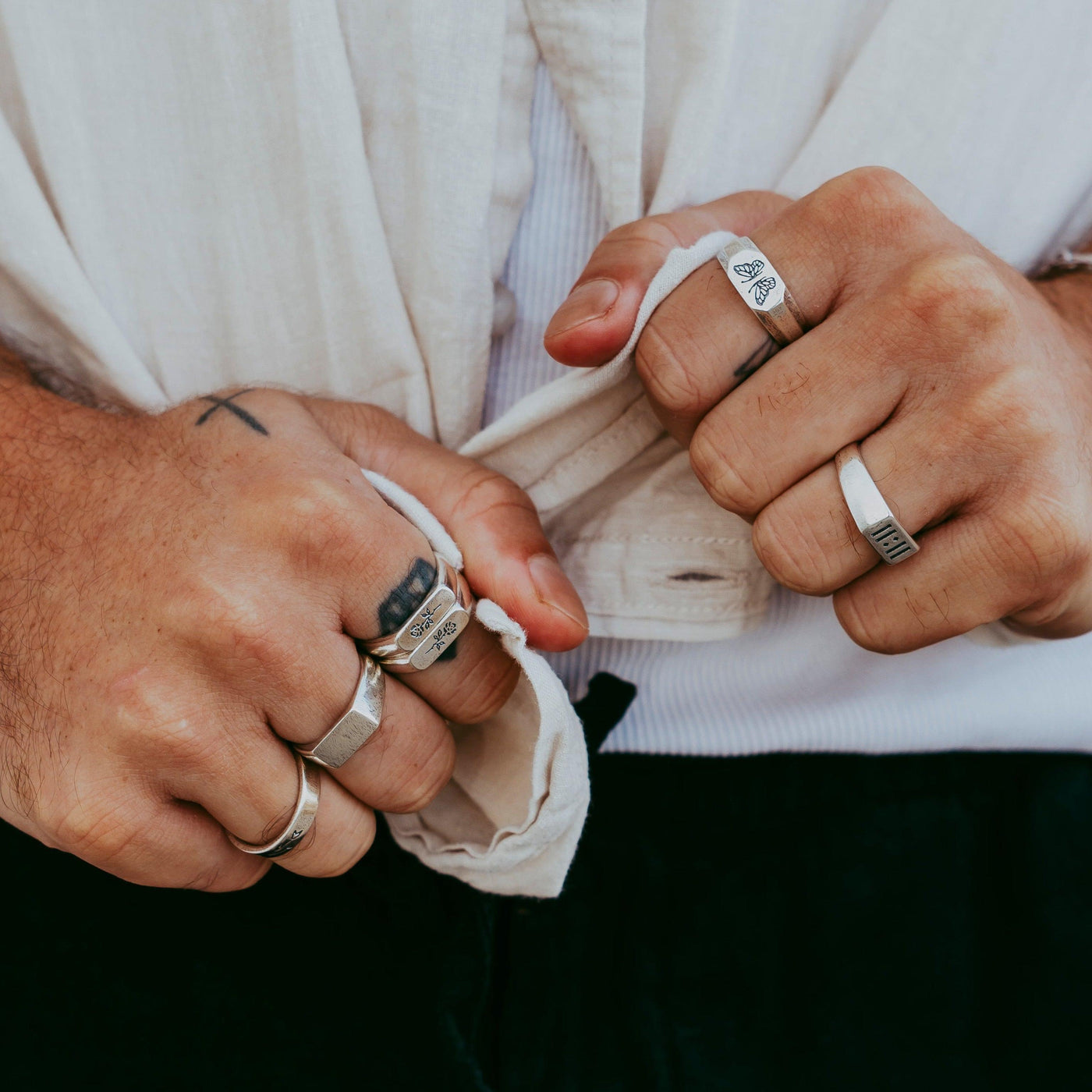 A close-up of a man's hands with tattoos, wearing a stack of sterling silver rings from Billie Jo, including the Genesis Ring. A stylish example of men's jewellery from this Australian brand.