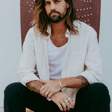 A male model sits wearing the sterling silver Persona Bracelet by Billie Jo, paired with multiple rings and a casual, layered outfit for a modern look.