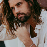 A male model with long brown hair wears the sterling silver Persona Bracelet from Billie Jo, styled with a casual, unbuttoned shirt for a relaxed look.