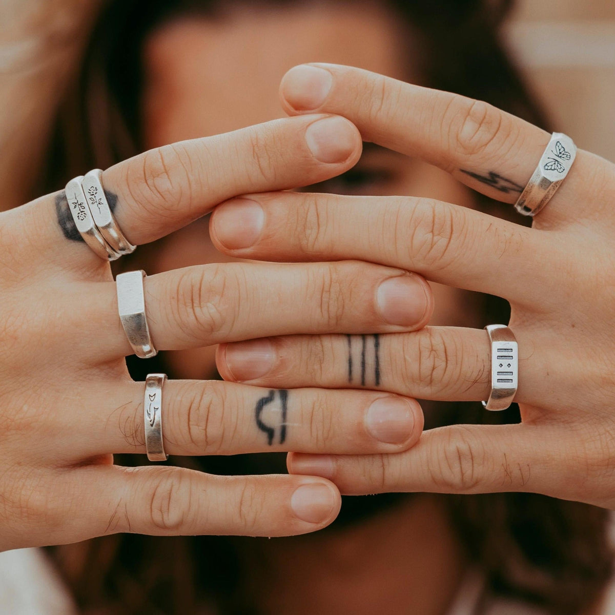 A close-up shot of a model's hands with multiple rings, including the ROSA I RING, showcasing the brand's modern and editorial aesthetic.
