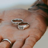 A close-up lifestyle shot showing two sterling silver Billie Jo rings, including the Prowess Ring, resting in the palm of a hand with a blurred beach background.