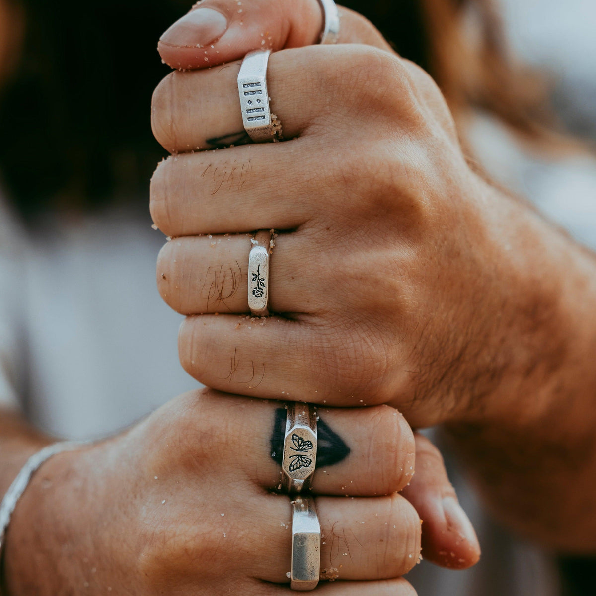 A close-up of a man's hands wearing a collection of sterling silver rings, including the Billie Jo Genesis Ring. A perfect example of how to stack men's jewellery for a modern, masculine look.
