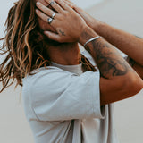 A man with his hands covering his face, showing off the sterling silver Persona Bracelet from Billie Jo on his wrist, along with several rings.
