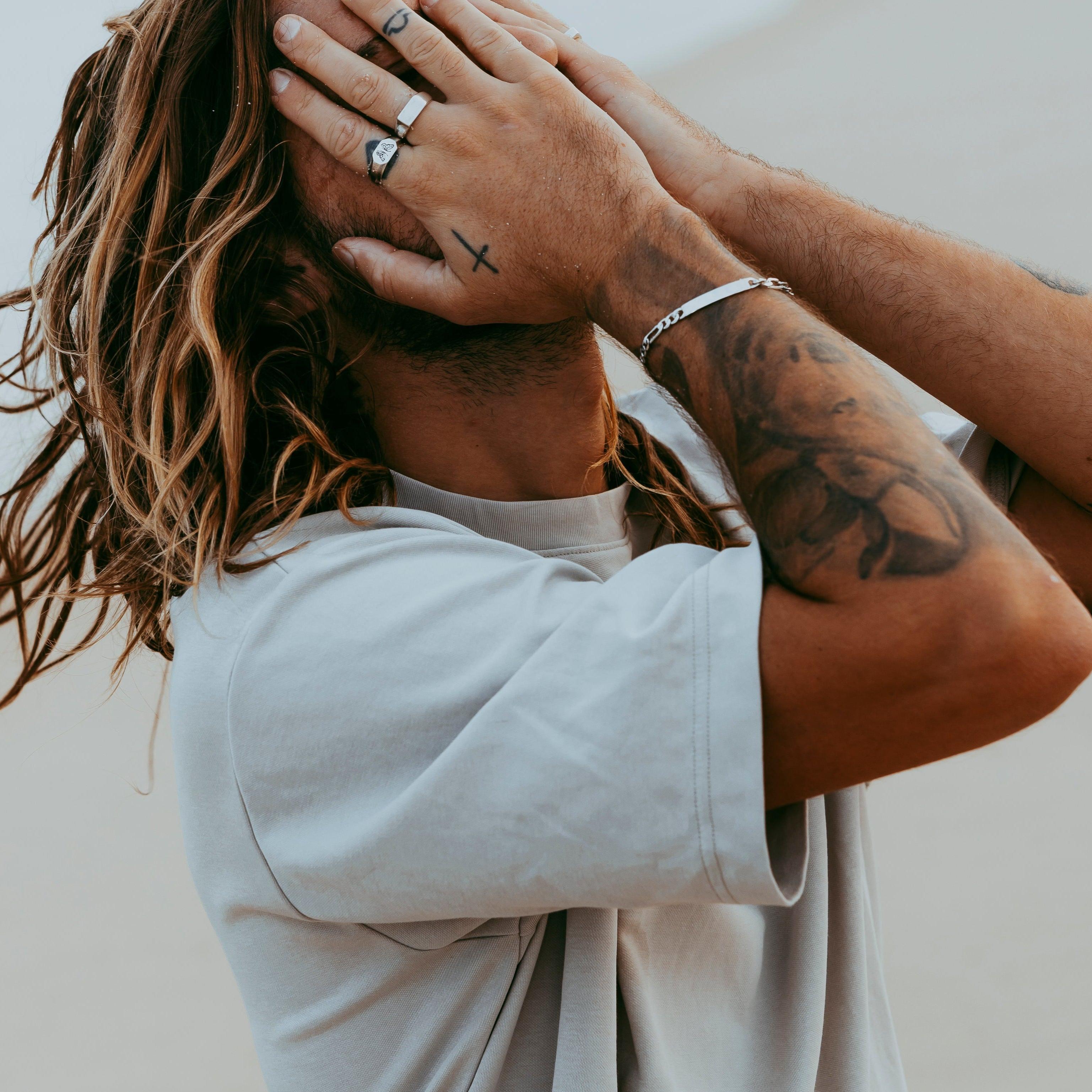 A man with his hands covering his face, showing off the sterling silver Persona Bracelet from Billie Jo on his wrist, along with several rings.