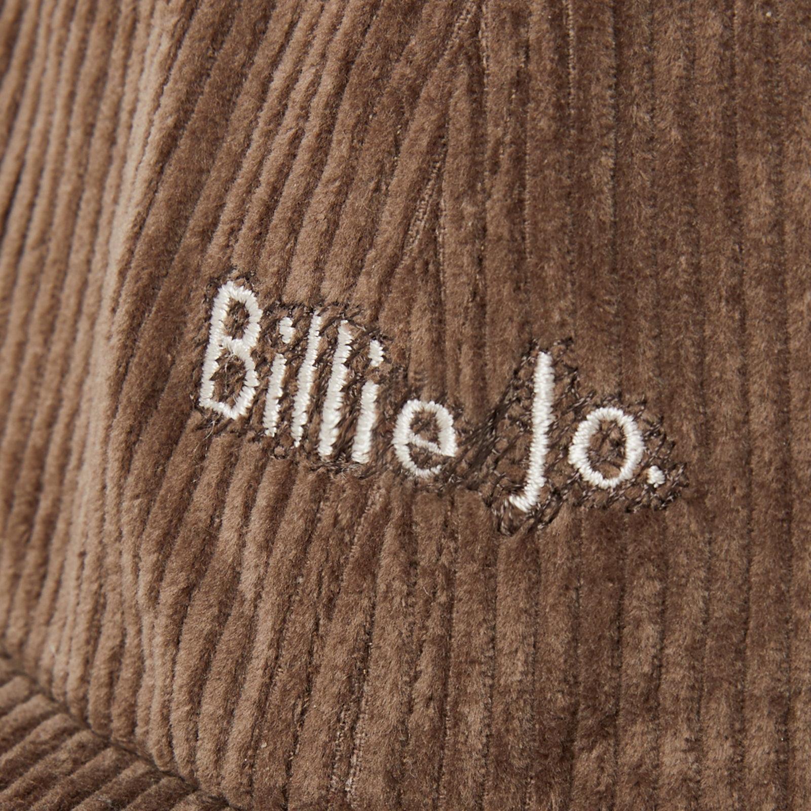 A macro shot of the 'Billie Jo' logo embroidered in white on the rich brown corduroy of the Corduroy Hat, showcasing the texture and quality.