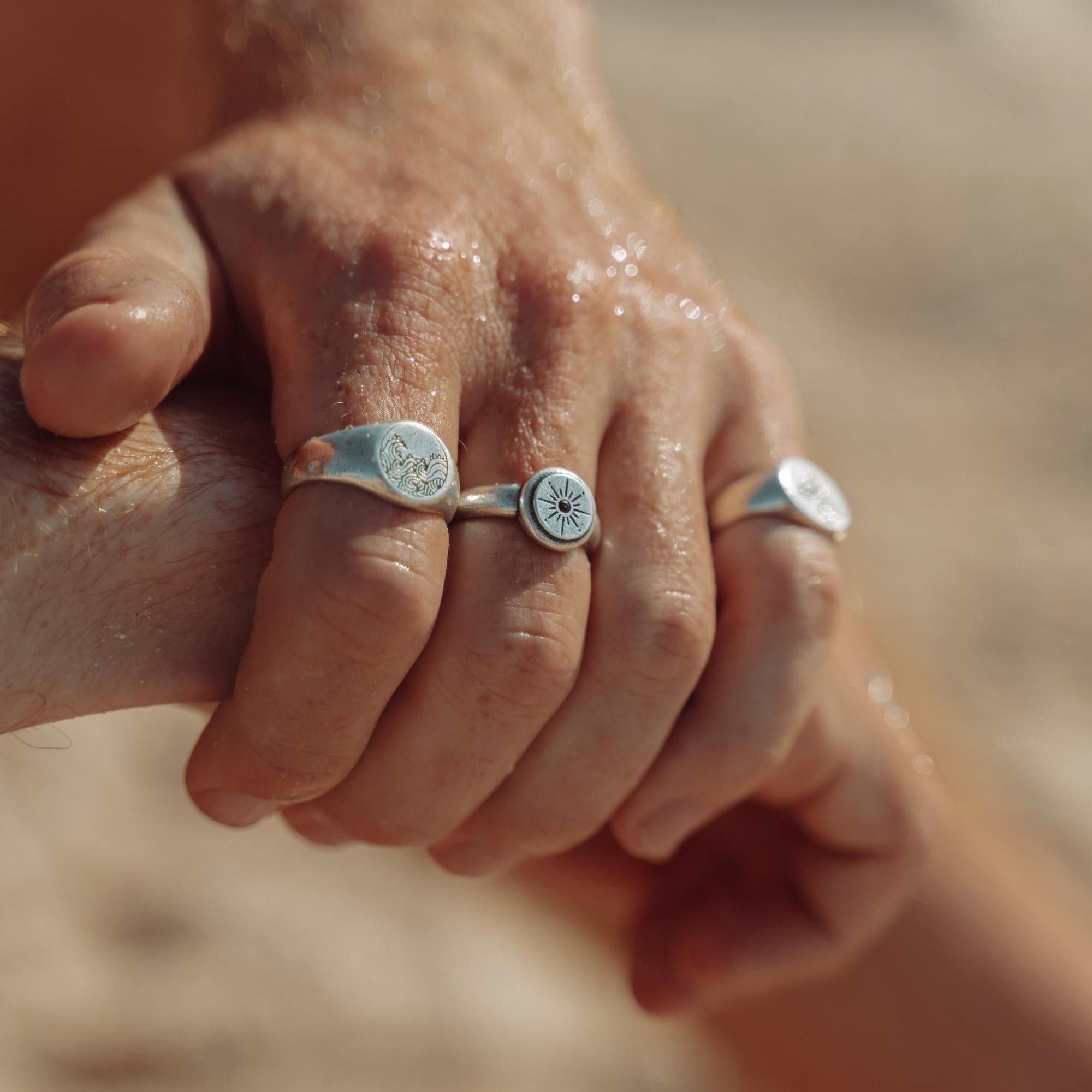 A sun-drenched, on-hand shot of a man wearing the Billie Jo Oracle Ring and other sterling silver pieces at the beach. This editorial image captures the essence of the Gold Coast lifestyle, with a focus on modern men\s jewellery.